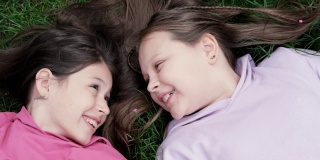 两个漂亮的千禧一代朋友躺在公园或草坪上的绿草地上。白人女孩笑着一起玩。俯视图