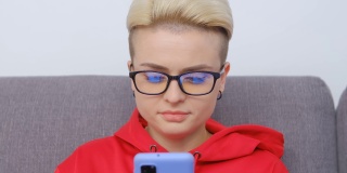 漂亮的假小子女人戴着眼镜用手机。视频肖像有吸引力的白人女性染短头发浏览互联网和社交媒体上的现代智能手机gadget