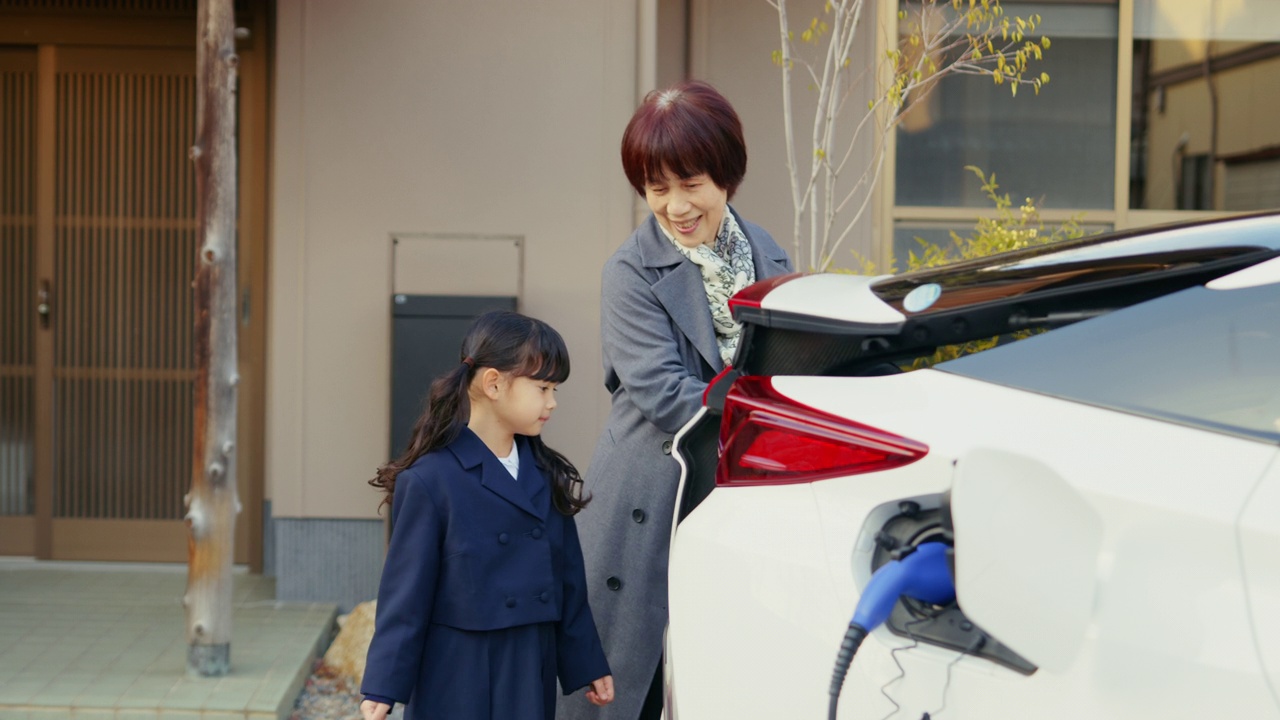 MS-一个年轻的女孩正在帮助她的祖母从他们的电动汽车上卸下购物的东西