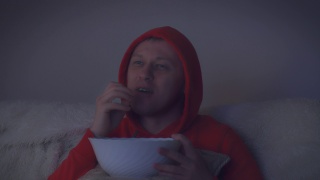 戴兜帽的男人在晚上看一部有趣的电影，用大碗吃薯片视频素材模板下载