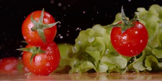 宏观:鲜红色的番茄落下，落在潮湿的长叶莴苣叶子上。
