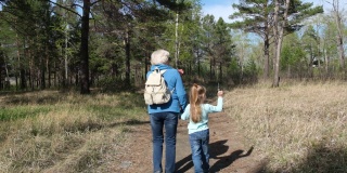 奶奶带着孙女走在小路上。在公园或森林里散步放松。两代人的家庭。