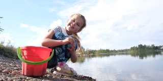 小女孩在沙滩上玩耍，往河里扔石头。研究大自然的细节。