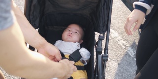 亚洲华人父母在去公园前要为他们的孩子系好婴儿车的安全带
