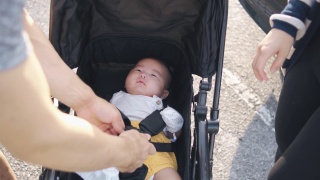 亚洲华人父母在去公园前要为他们的孩子系好婴儿车的安全带视频素材模板下载