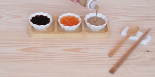 三种酱汁，白色杯子放在竹制的架子上，筷子和勺子放在木制的桌子背景上。