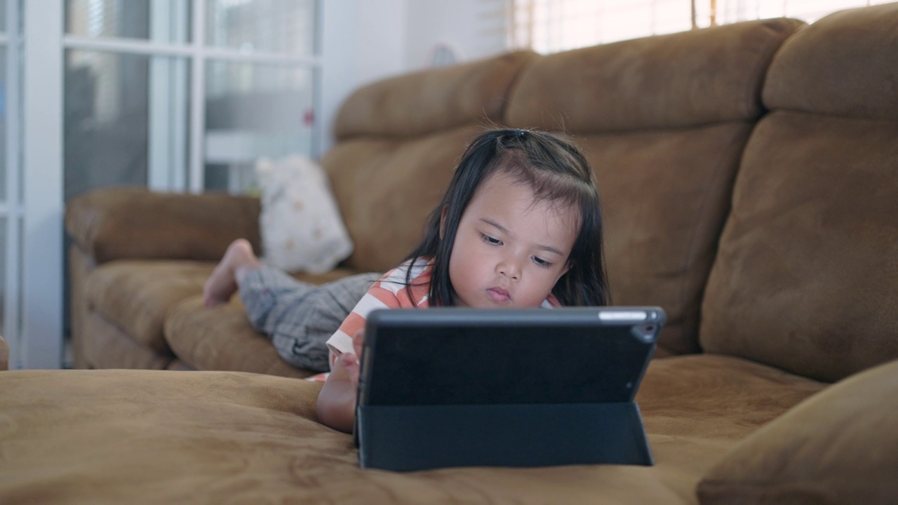 一个亚洲小女孩躺在沙发上喜欢看平板电脑