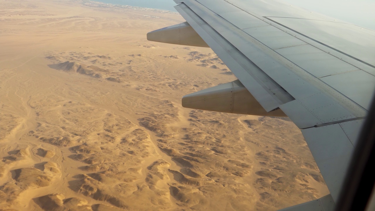 飞机飞过沙漠，从飞机机翼上的舷窗和襟翼上看到的景象。