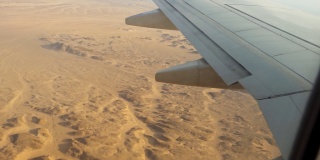 飞机飞过沙漠，从飞机机翼上的舷窗和襟翼上看到的景象。