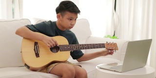 亚洲男孩在笔记本电脑上通过网络视频与老师在线学习音乐。