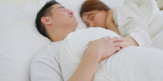 亚洲有吸引力的年轻夫妇躺在床上睡觉在卧室。美丽的新婚夫妇，穿着睡衣的男人和女人，清晨在房子里一起躺在舒适的枕头上，感到幸福和放松。