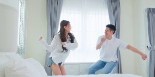 亚洲年轻情侣在家里的卧室里一起随着音乐跳舞。迷人浪漫的新婚男女享受清晨醒来后在屋里花时间听和唱歌