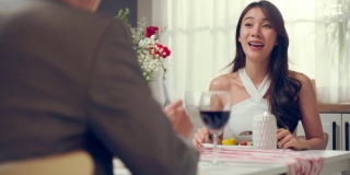 亚洲年轻情侣共进晚餐庆祝情人节。迷人的新婚男女享受夜晚的派对，在结婚纪念日喝一杯红酒，幸福的在家。