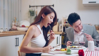 亚洲年轻情侣共进晚餐庆祝情人节。迷人浪漫的新婚男女在家里的厨房里举行晚会，在餐桌上吃结婚纪念日的食物。视频素材模板下载
