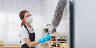 亚洲清洁服务女工清洁厨房和家庭。漂亮的女管家清洁工戴着口罩，用鸡毛掸子擦拭凌乱的柜台，为管家做家务或杂务。
