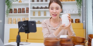 亚洲美女在家在线直播卖花瓶产品。年轻漂亮的女孩用笔记本电脑向顾客展示商品并呈现细节。远程购买和购买购物概念
