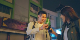 亚洲帅哥情侣一起喝酒开派对。在城市里旅游的青年男女，在假期里一起拿着一瓶啤酒，在漆黑的夜晚在路上度过时光。