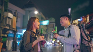 亚洲帅哥情侣一起喝酒开派对。在城市里旅游的青年男女，在假期里一起拿着一瓶啤酒，在漆黑的夜晚在路上度过时光。视频素材模板下载