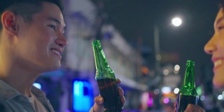 亚洲帅哥情侣一起喝酒开派对。在城市旅游的年轻男女在假期的夜晚一起在路上碰碰啤酒