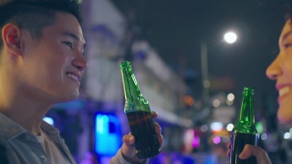 亚洲帅哥情侣一起喝酒开派对。在城市旅游的年轻男女在假期的夜晚一起在路上碰碰啤酒视频素材模板下载
