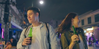 亚洲帅哥情侣一起喝酒开派对。在城市里旅游的青年男女，在假期里一起拿着一瓶啤酒，在漆黑的夜晚在路上度过时光。
