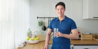 亚洲有吸引力的男性的肖像，在厨房里拿着一杯水。年轻饥渴的帅哥在清晨醒来后，为居家保健而斟上一杯纯净的天然矿物质