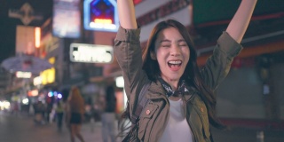 亚洲女游客在旅行时感到宿醉，在街上跳舞。美丽的背包女孩独自旅行在夜间的路，拿着一瓶啤酒，在假日度假旅行在泰国喝。