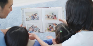亚洲家庭看着旧相册上的照片回忆过去。年轻漂亮的夫妇和年幼的女儿坐在一起，翻动着相册，享受着回忆彼此关系的时光。