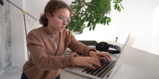 一个严肃的少女若有所思地看着笔记本电脑屏幕打字的特写镜头。远程教育技术和家庭作业