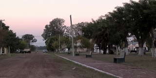 阿根廷恩特雷里奥斯省的一个小村庄里，日落时分，土路旁的一个空公园里有石凳。