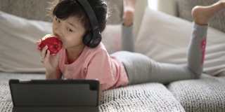 小女孩在家里的客厅里用数码平板电脑在线学习