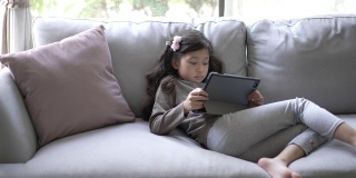 小女孩在家里的客厅里用数码平板电脑在线学习