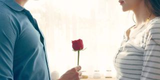 亚洲青年惊喜送玫瑰给美丽的女友。迷人浪漫的新婚男女花时间在房子里一起庆祝周年纪念日和情人节。