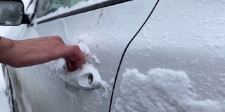 在冬天的早晨，一名无法辨认的男性司机用手清理车门把手上的新雪。