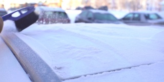 在一个阳光明媚的冬日里，一位戴着手套的无法辨认的女司机用刷子清理车顶上刚下过的雪。