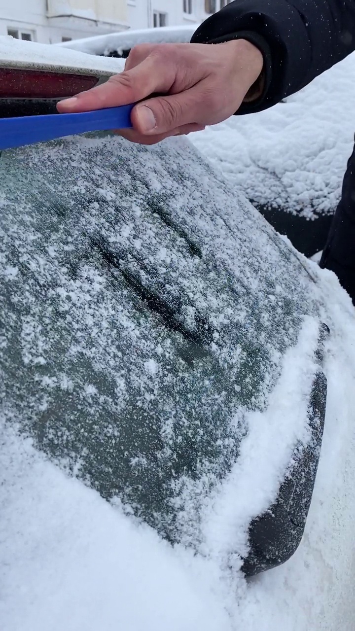 在一个冬天的早晨，一名无法辨认的男性司机正在用刷子清理汽车后窗上的新雪。