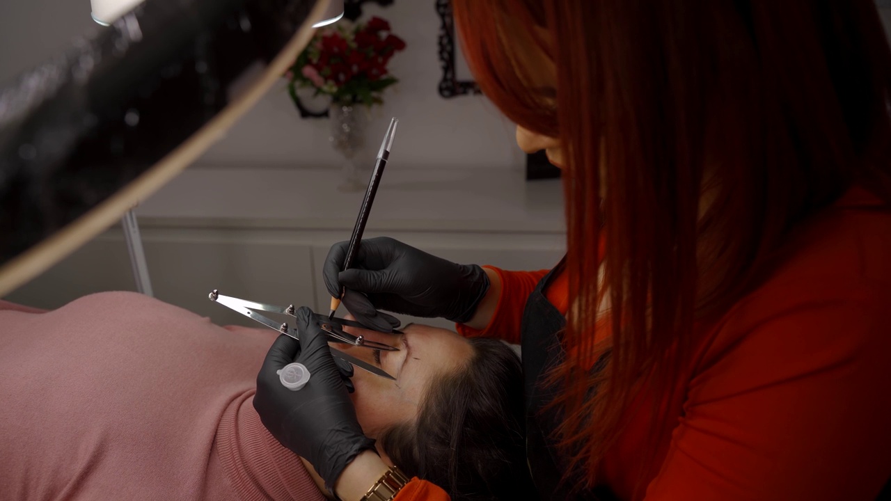 主美容师的手的侧面视图测量眉毛的比例，用特殊的工具涂上颜料。microblading的概念