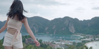 年轻活跃的亚洲女孩跳舞在山顶俯瞰美丽的岛屿观点，自由的生活方式逃离繁忙拥挤的城市，遥远的夏季岛屿跳旅行者