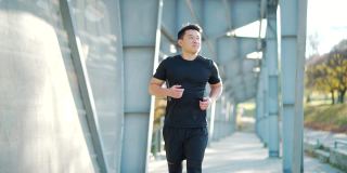年轻的亚洲跑步者在现代城市体育场的背景下跑步。晨跑运动穿着黑色运动服的运动员。沿着城市的街道慢跑。