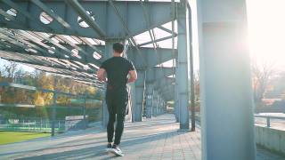 年轻的亚洲男子跑步在城市体育场的城市背景的街道上。穿着黑色运动服晨跑积极健康的生活方式视频素材模板下载