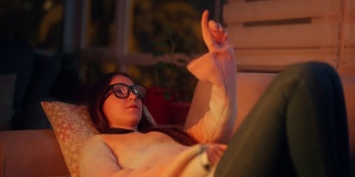 美丽的女人躺在沙发上的肖像和使用智能眼镜。元境智能眼镜虚拟现实技术概念