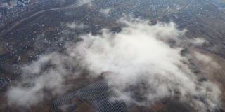 高空鸟瞰图，远处的城市被暴雨前形成的蓬松的积云所覆盖。飞机角度多云的景观