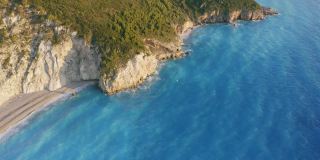 鸟瞰希腊爱奥尼亚岛莱夫卡达美丽的米洛斯海滩。日落金色的阳光，悬崖般的海岸线和原始的海浪打破了蓝绿色的大海在岸边