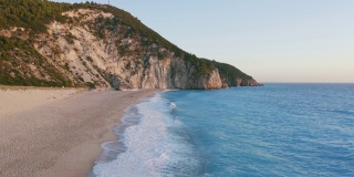 鸟瞰希腊爱奥尼亚岛莱夫卡达美丽的米洛斯海滩。夕阳金色的阳光和原始的海浪打破了蓝绿色的大海在岸边