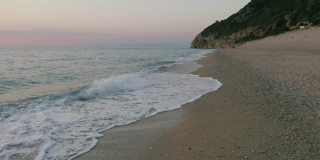 鸟瞰希腊爱奥尼亚岛莱夫卡达美丽的米洛斯海滩。夕阳金色的阳光和原始的海浪打破了蓝绿色的大海在岸边