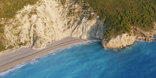 鸟瞰希腊爱奥尼亚岛莱夫卡达美丽的米洛斯沙滩。夕阳金色的阳光和原始的海浪打破了蓝绿色的大海在岸边