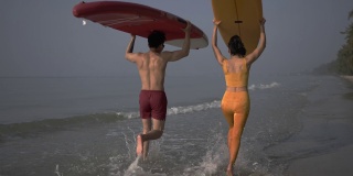 带着冲浪板冲进海浪的快乐夫妇。