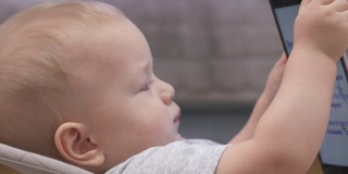 可爱的白人小孩坐在摇椅上看动画片，9个月大的婴儿抱着平板电脑在家。儿童和移动技术。