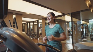 亚洲妇女在健身房的跑步机上跑步视频素材模板下载