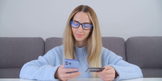 年轻的金发女人用现代智能手机和银行卡在4k股票视频在线购物。白人女性用手机转账